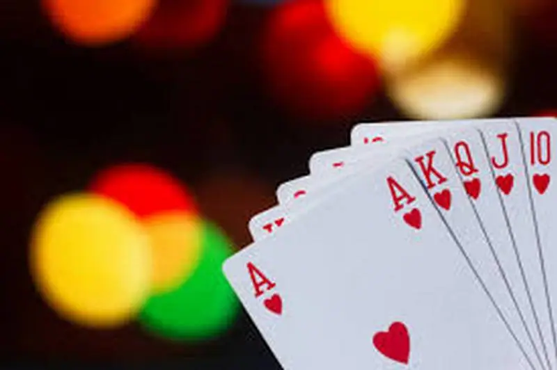A royal flush in hearts, ace to ten, held in front of blurred coloured lights